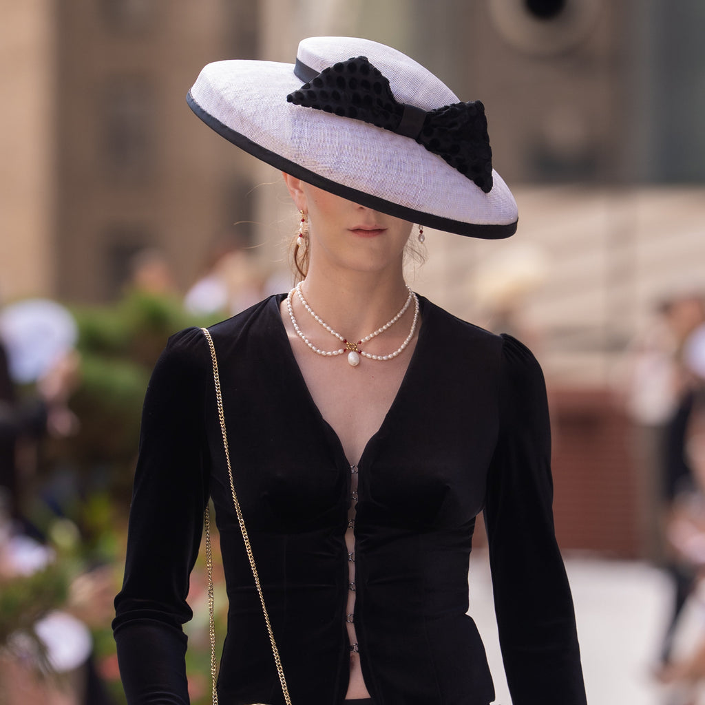 A romantic, vintage inspired necklace that features real freshwater pearls, red crystals, and 18k real gold plated beads. It is being worn by a model during New York Fashion Week. 