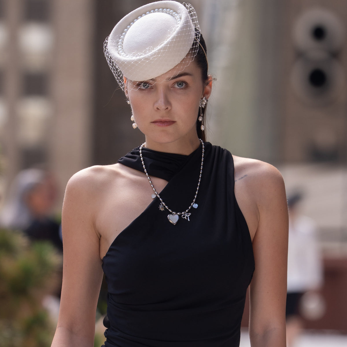A charm necklace featuring a locket with a mother of pearl face. Being worn by a model at New York Fashion Week. 