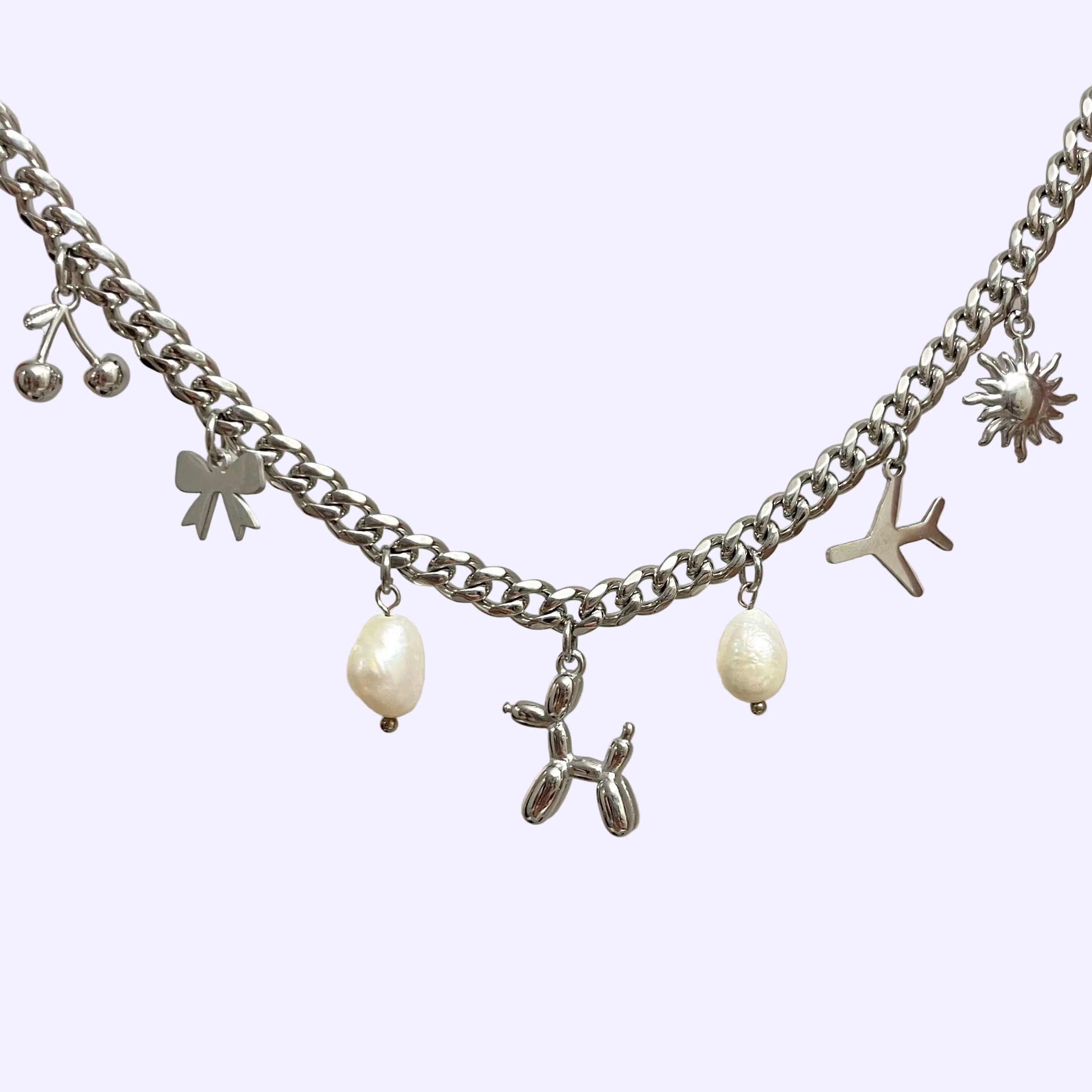 Silver chain necklace with various charms on a light gray background.