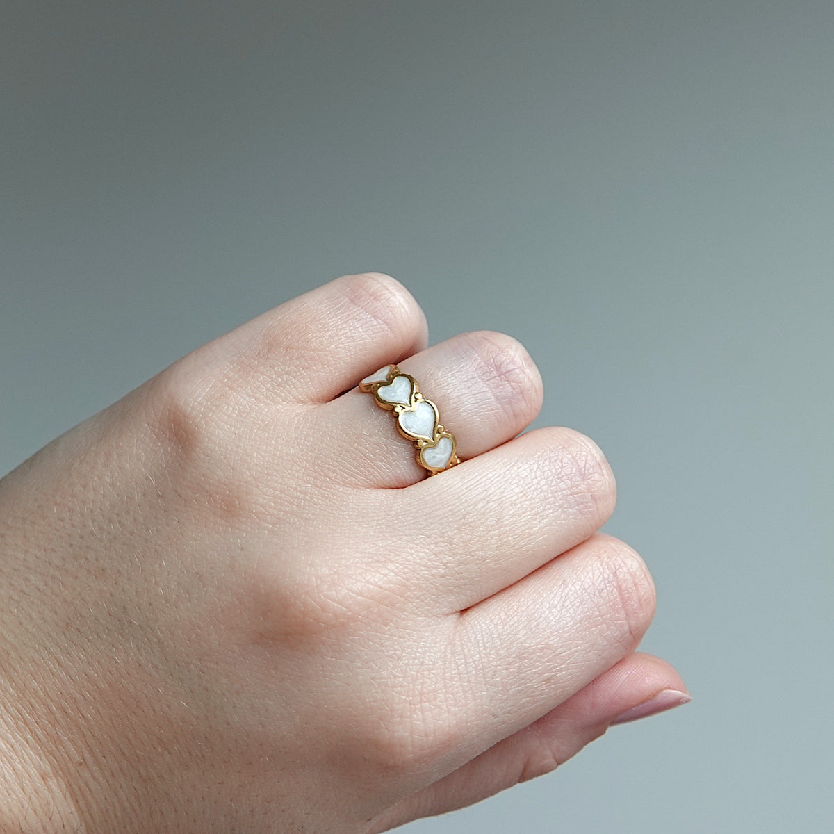 Hand wearing a gold ring with heart-shaped pearls on a gray background